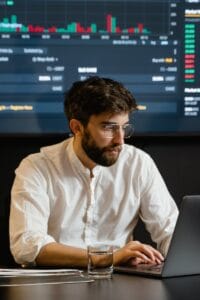 Professional analyzing stock market trends using laptop and digital display in modern office.